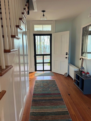 A hallway with a wooden floor, a patterned rug, a white door, and a radiator.