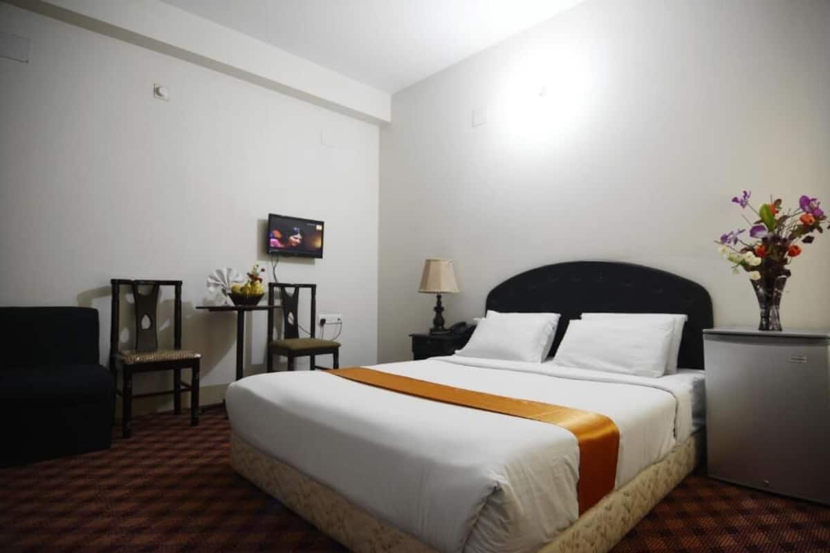 Une chambre d’hôtel équipée d’un lit, d’un bureau, d’une chaise, d’une lampe et d’un petit réfrigérateur.