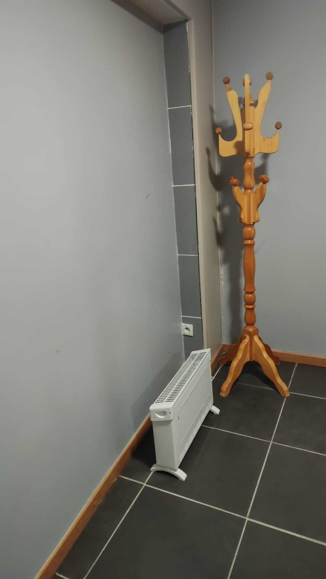 Eine Ecke mit Heizkörper, einem Holz-Kleiderständer und Fliesenboden.