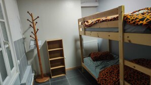 Une chambre avec un lit superposé, un porte-manteau, une petite étagère et un radiateur.