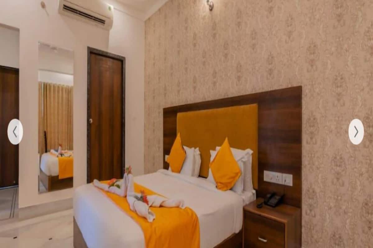 A hotel room with a large bed, a wooden headboard, a nightstand with a phone, and a mirror on the wall.