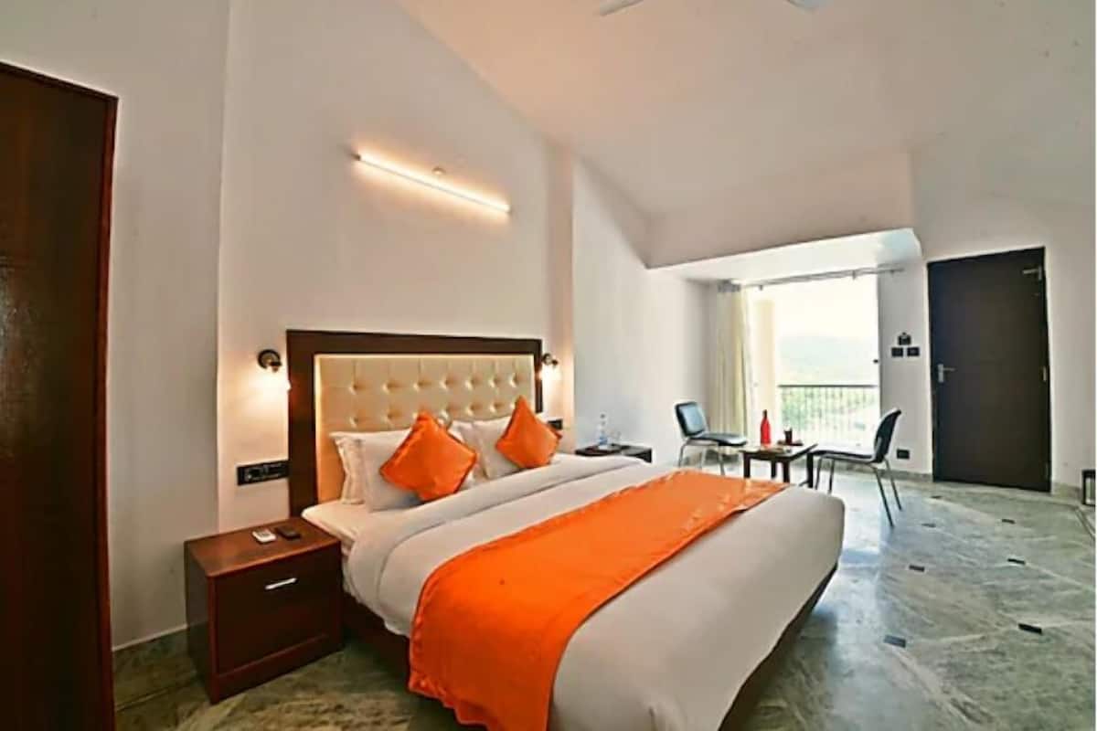 A hotel room with a large bed, a nightstand, a desk with a chair, and a balcony with a view.
