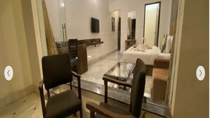A modern living room with a glass coffee table, two armchairs, a sofa, and a TV mounted on the wall. - Mewar Palace Resort & Spa (Udaipur)