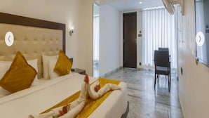 A hotel room with a bed, a bedside table, a wall-mounted fan, and a door leading to another room. - Mewar Palace Resort & Spa (Udaipur)