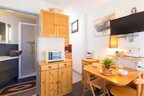 A compact kitchen with wooden cabinets, a microwave, a coffee maker, and a dining area with a table and chairs. - Studio 2 ppl, near the ski runs (Les Deux Alpes)