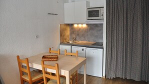 Une cuisine compacte équipée d’un évier, d’un lave-vaisselle et d’un four à micro-ondes. On y trouve une table à manger avec des chaises, et un panier posé dessus.