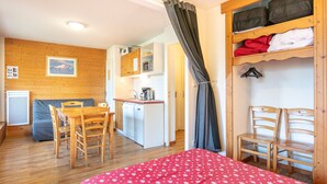 Quarto compacto com cama, mesa de jantar com cadeiras, cozinha compacta e armário de madeira.