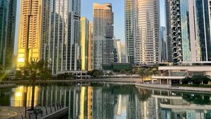 A modern cityscape with high-rise buildings and a calm water body reflecting the structures. - Cozy 2 bedroom near metro in JLT (Dubai)