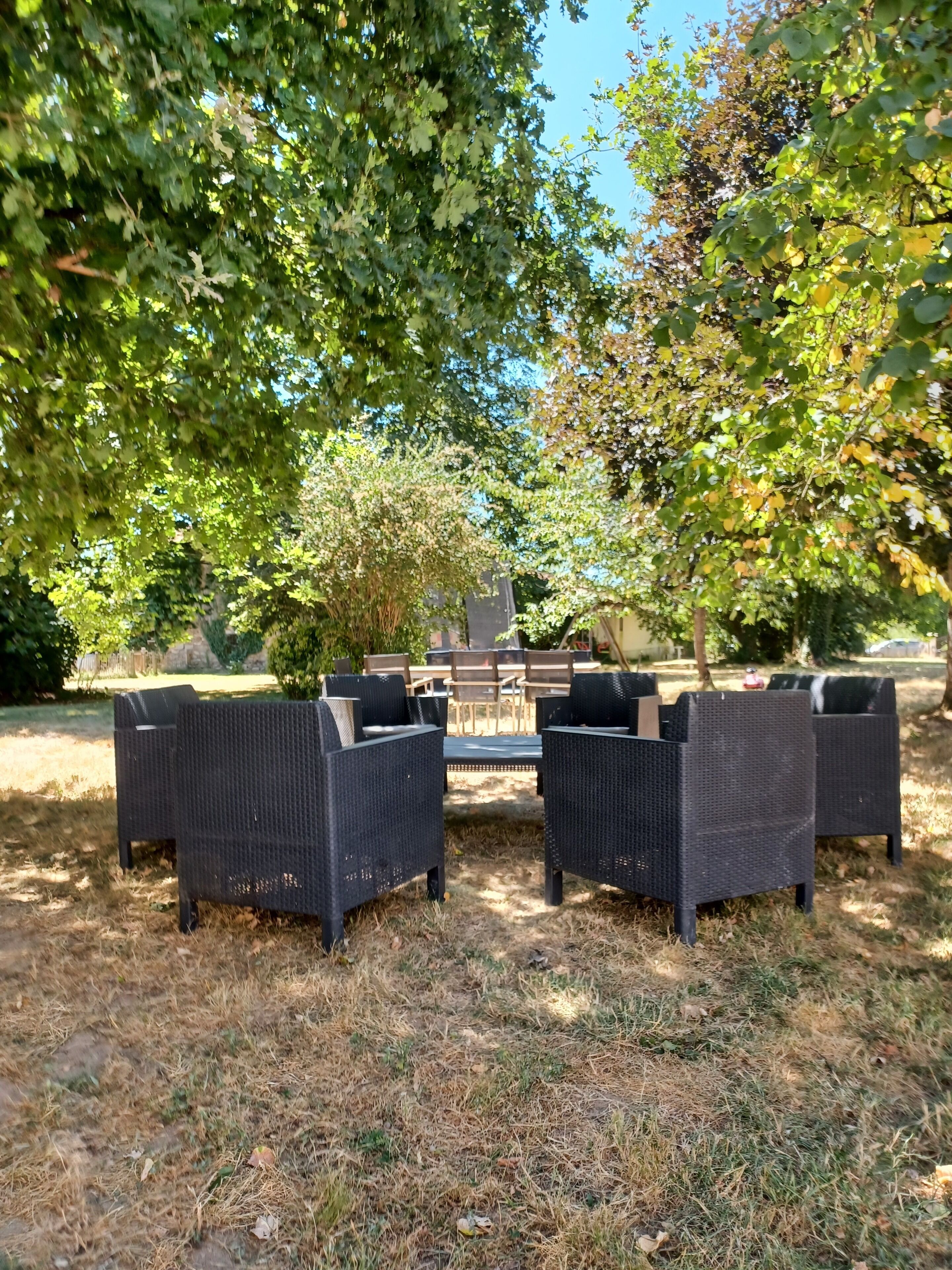 An outdoor seating area with wicker furniture, surrounded by trees and a grassy lawn.