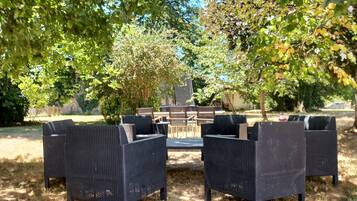 An outdoor seating area with wicker furniture, surrounded by trees and a grassy lawn.
