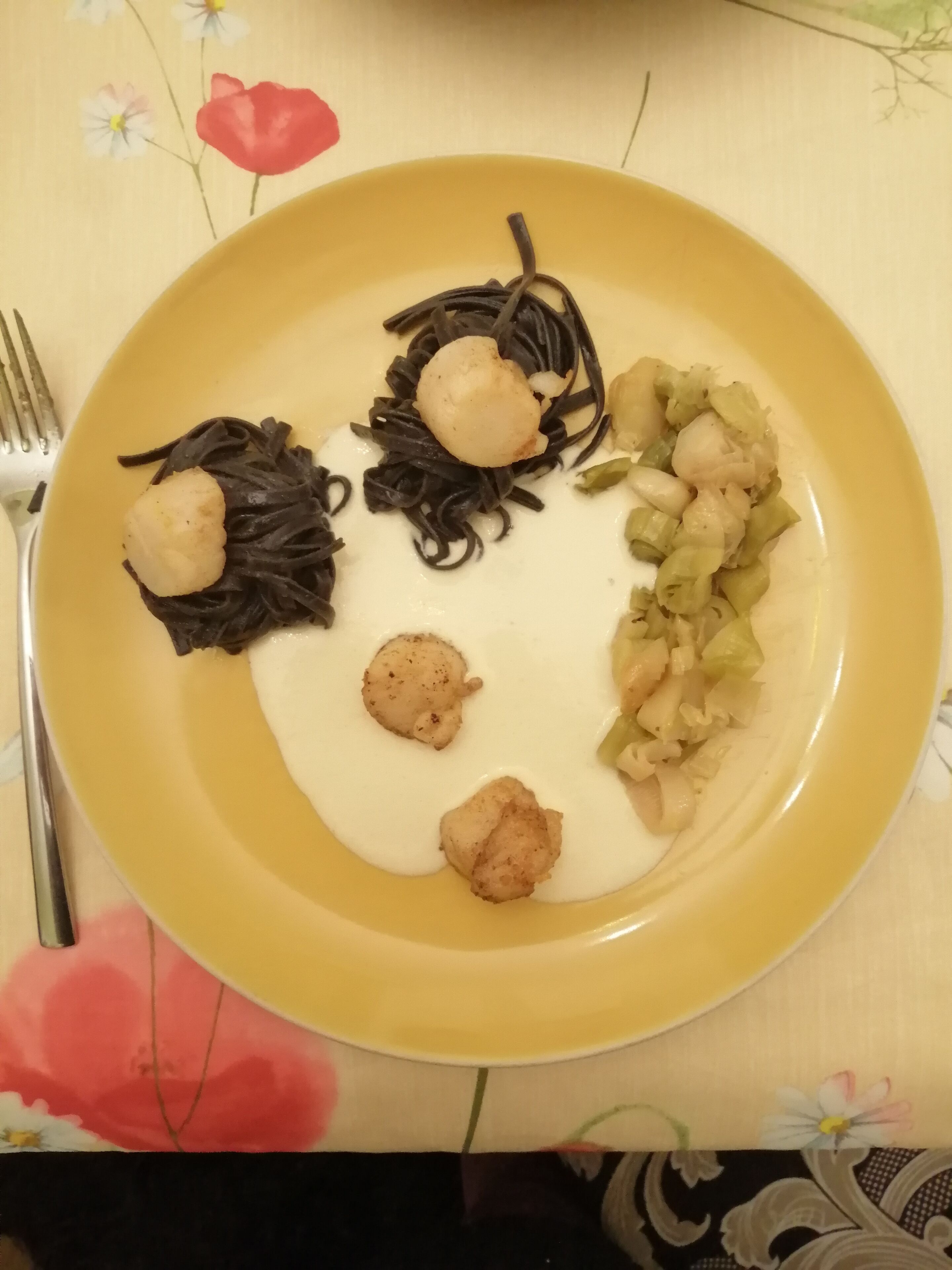 Un plato con fideos negros, vieiras y una guarnición de vegetales encurtidos.
