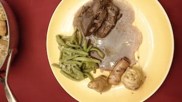Un plato amarillo con un palillo de cordero, judías verdes y champiñones sobre una mesa roja.