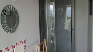 Une salle de bain avec une douche à parois de verre, un lavabo blanc avec un porte-savon, une chaise en bois et un miroir au mur.