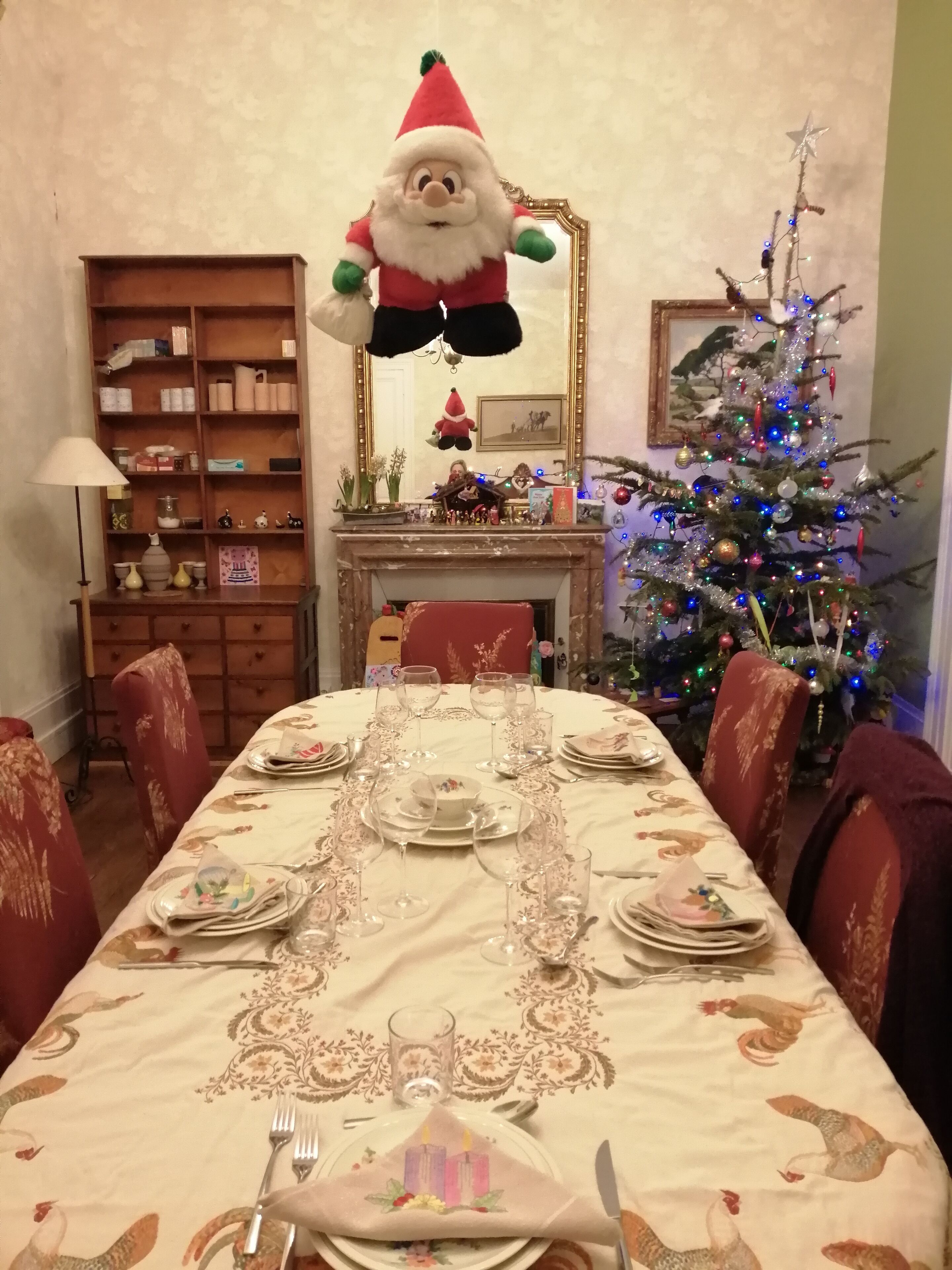 A dining room with a long table set for a meal, a Christmas tree, and a Santa Claus decoration.