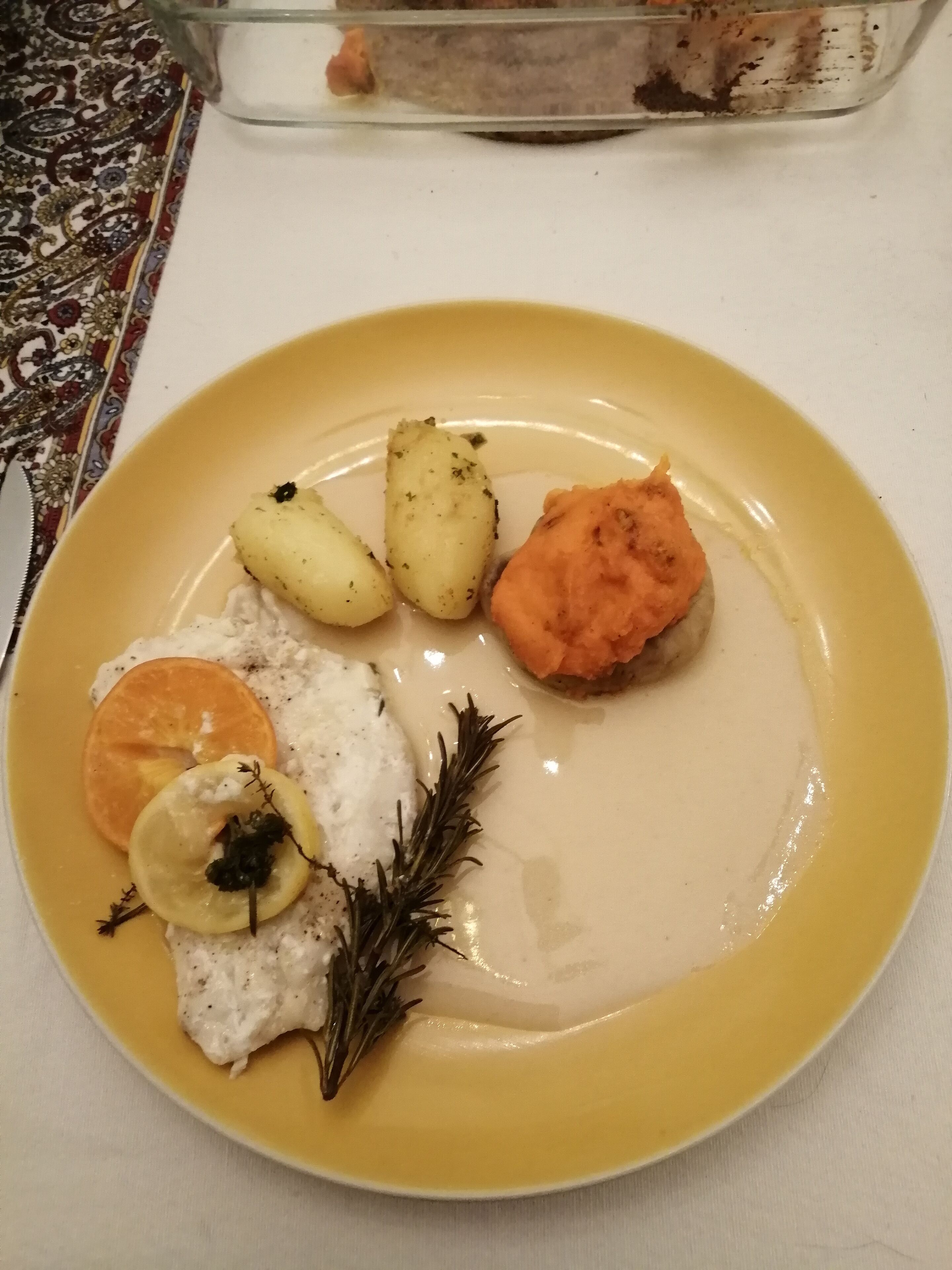 A plate with various food items including potatoes, a slice of orange, and a dollop of cream.