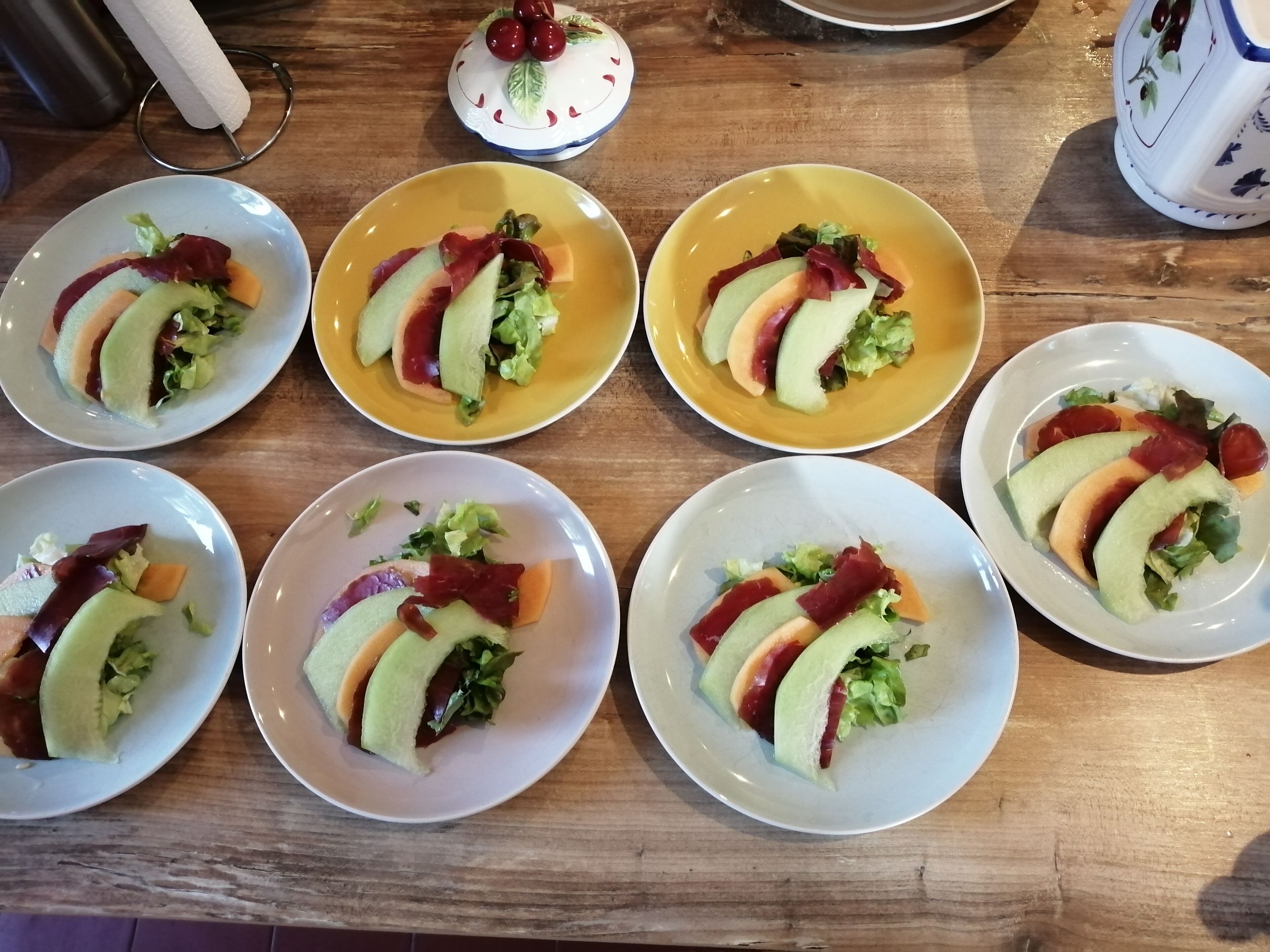 Een houten tafel met zes borden eten, elk met plakjes avocado, sla en rood vlees.