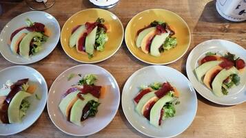 Een houten tafel met zes borden eten, elk met plakjes avocado, sla en rood vlees.