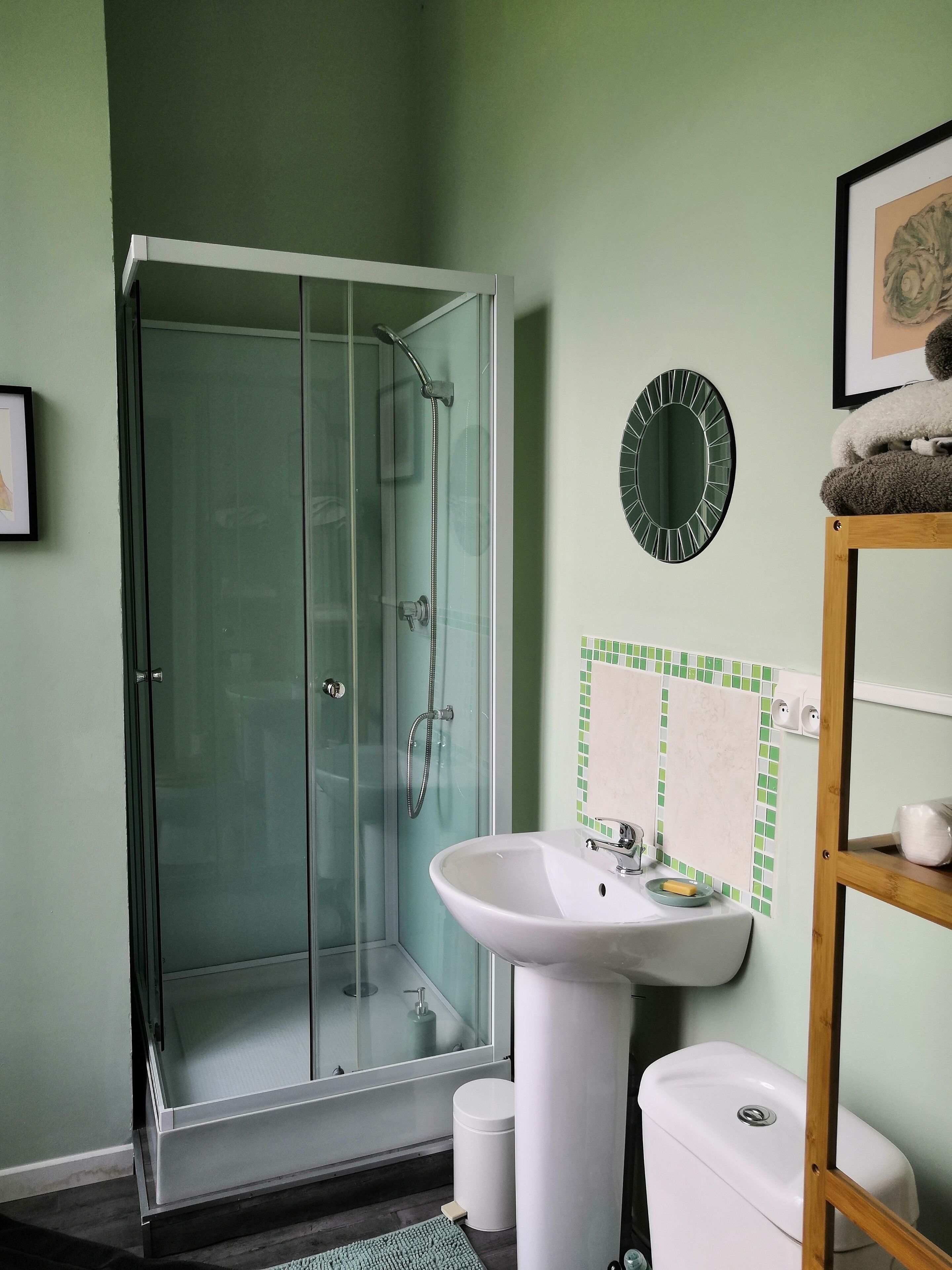 Een badkamer met een douchecabine van glas, een witte wastafel en een toilet.