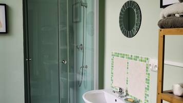 Een badkamer met een douchecabine van glas, een witte wastafel en een toilet.