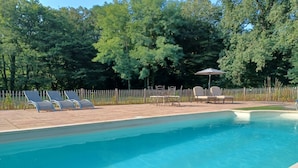 A swimming pool with lounge chairs and tables, surrounded by a wooden fence and trees.