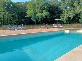 A swimming pool with lounge chairs and tables, surrounded by a wooden fence and trees.