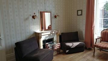 A room with a fireplace, two armchairs, a wooden floor, and a window with curtains.