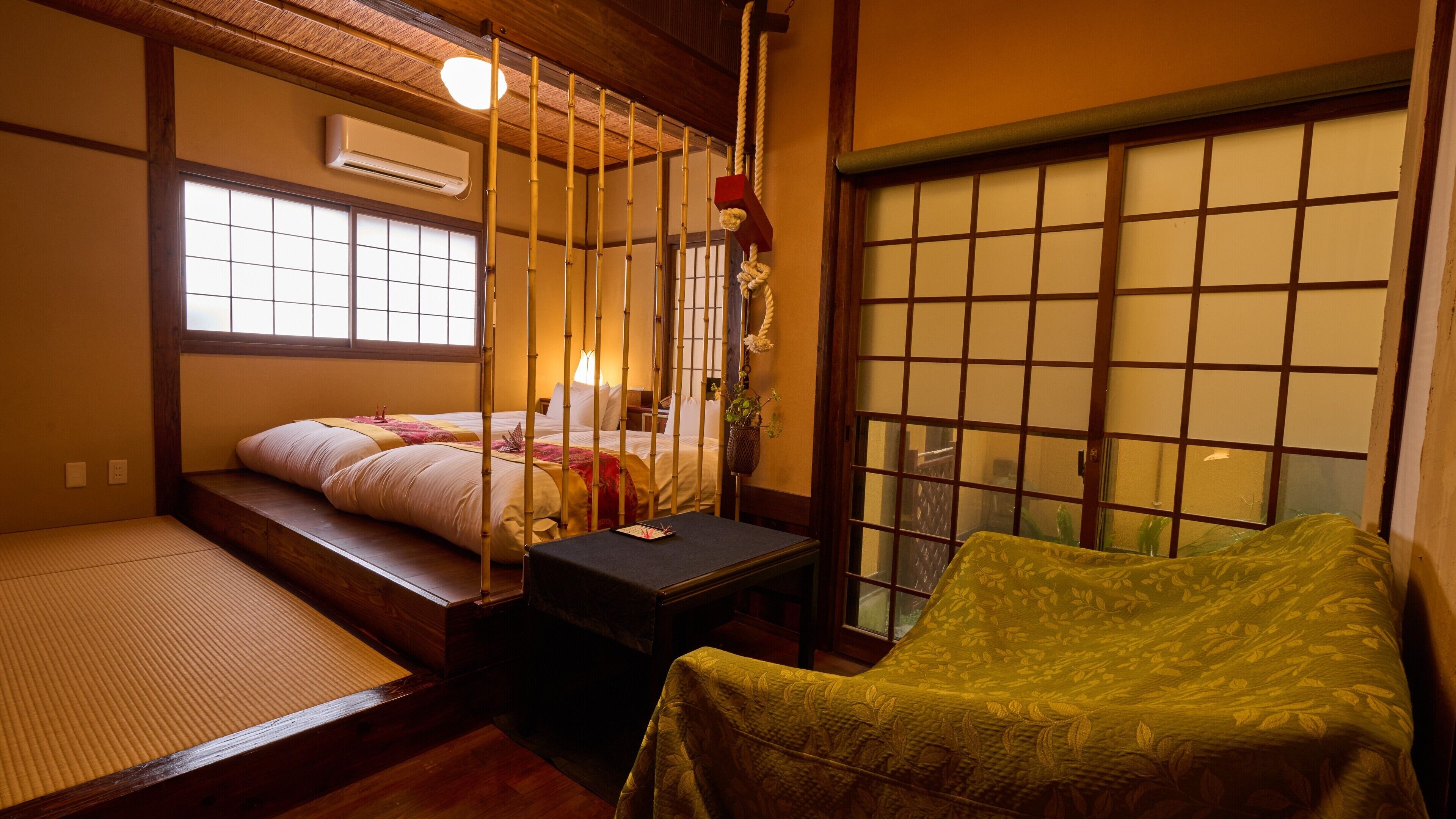 A traditional Japanese room with tatami flooring, a futon bed, a shoji screen, and a small table with a vase.