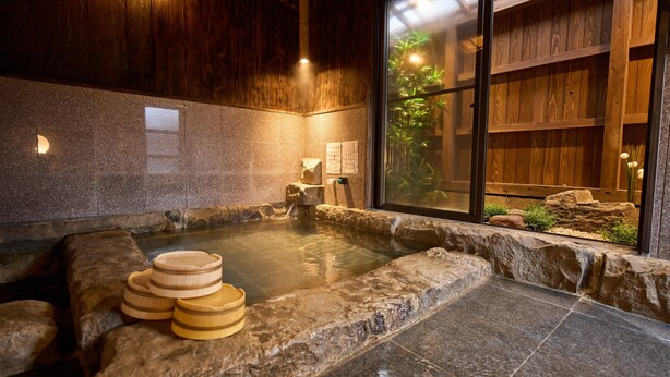A traditional Japanese onsen with a stone hot spring, wooden shelves, and a view of greenery through a glass door. - Kigannoyado Aoshima Jizoan (Miyazaki)