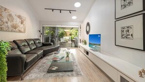 Ein modernes Wohnzimmer mit einer Ledersofa, einem Glastisch und einem Fernseher an einer weißen Wand.