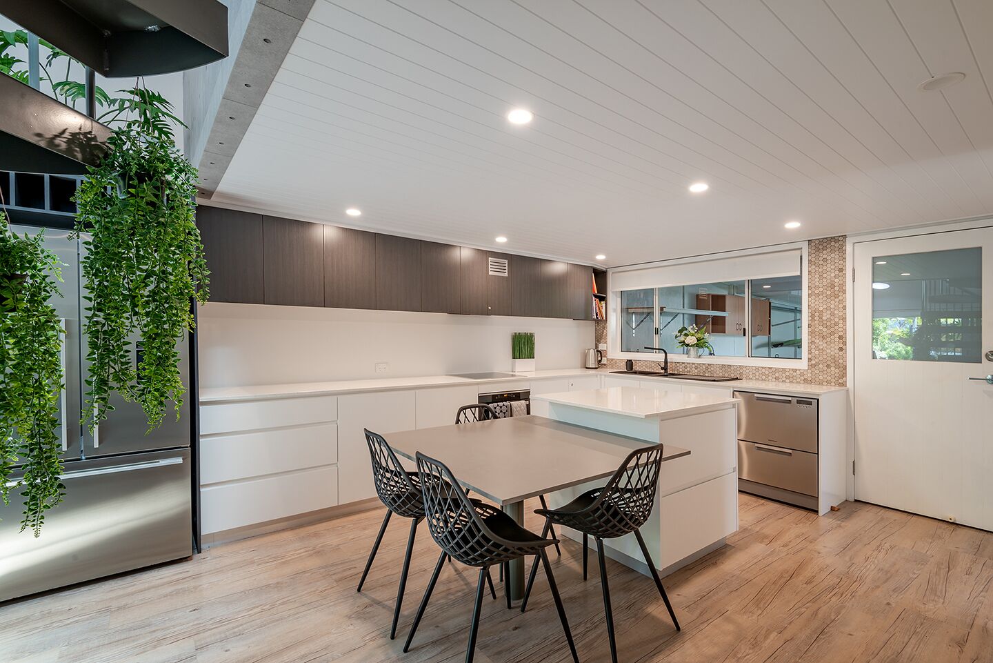 A modern kitchen with a central island, dark cabinetry, and a hanging plant.
