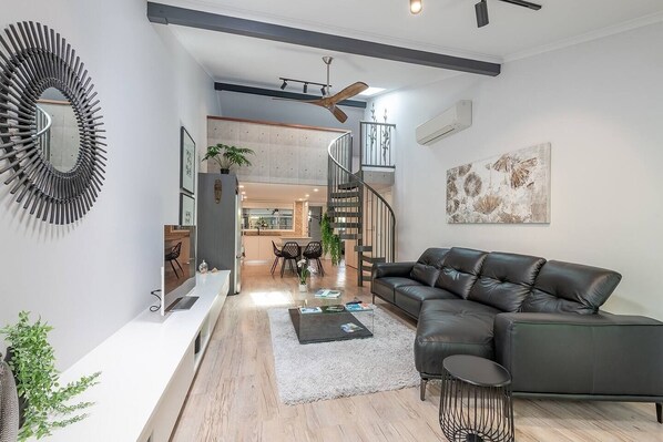 A modern living room with a black leather sofa, a white console table, a round mirror, and a staircase leading to an upper level.