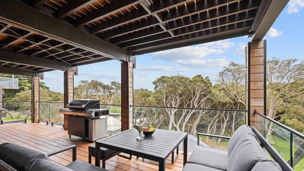 Une terrasse extérieure couverte, équipée d’un barbecue, d’un espace salon et offrant une vue sur les arbres environnants.