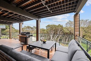 A covered outdoor deck with a grill, seating area, and a view of the surrounding trees. - Modern contemporary beach house in Sorrento with heated infinity pool & spa (Sorrento)