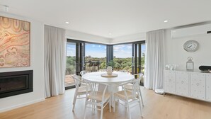 Une salle à manger moderne avec une table ronde, des chaises blanches et une vue sur l’extérieur.