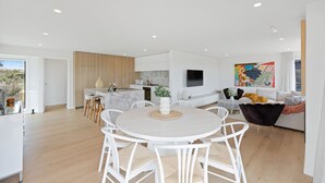 Une cuisine moderne avec des meubles blancs, un plan de travail en bois et un coin repas comprenant une table ronde et des chaises blanches.