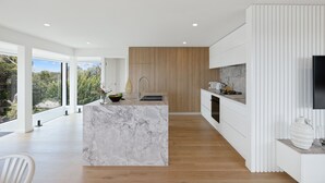 Une cuisine moderne dotée d’un îlot en marbre, de meubles en bois et d’une grande fenêtre donnant sur un espace verdoyant.