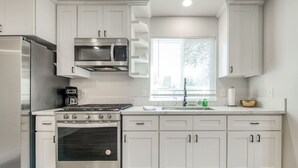 A modern kitchen with white cabinets, stainless steel appliances, and a window providing natural light. - Serene Space, Explore Nearby Attractions (Fresno)
