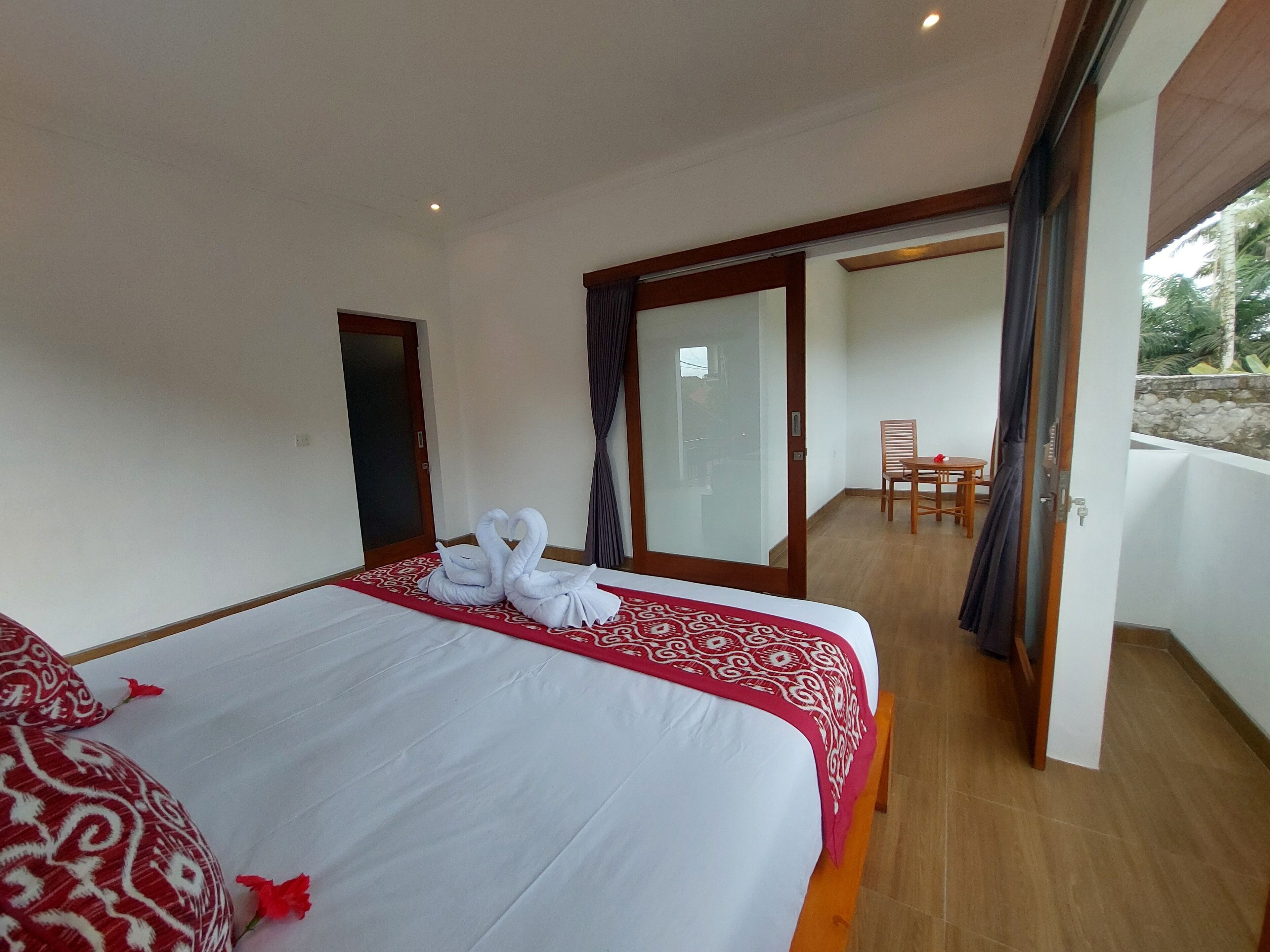 Une chambre d’hôtel avec un grand lit, un balcon avec une table et des chaises, et une porte-fenêtre coulissante.