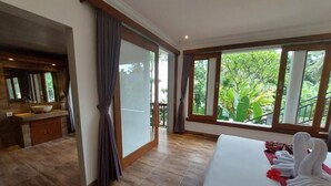 Ein Hotelzimmer mit einem großen Bett, einem Badezimmer mit einem Waschbecken und Blick auf Grün hinter großen Fenstern.