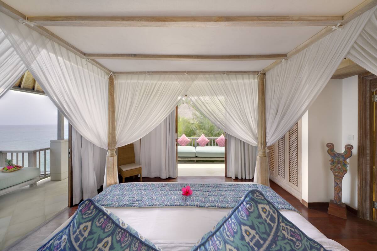 Quarto com cama grande, vista para o mar e varanda com sofá.