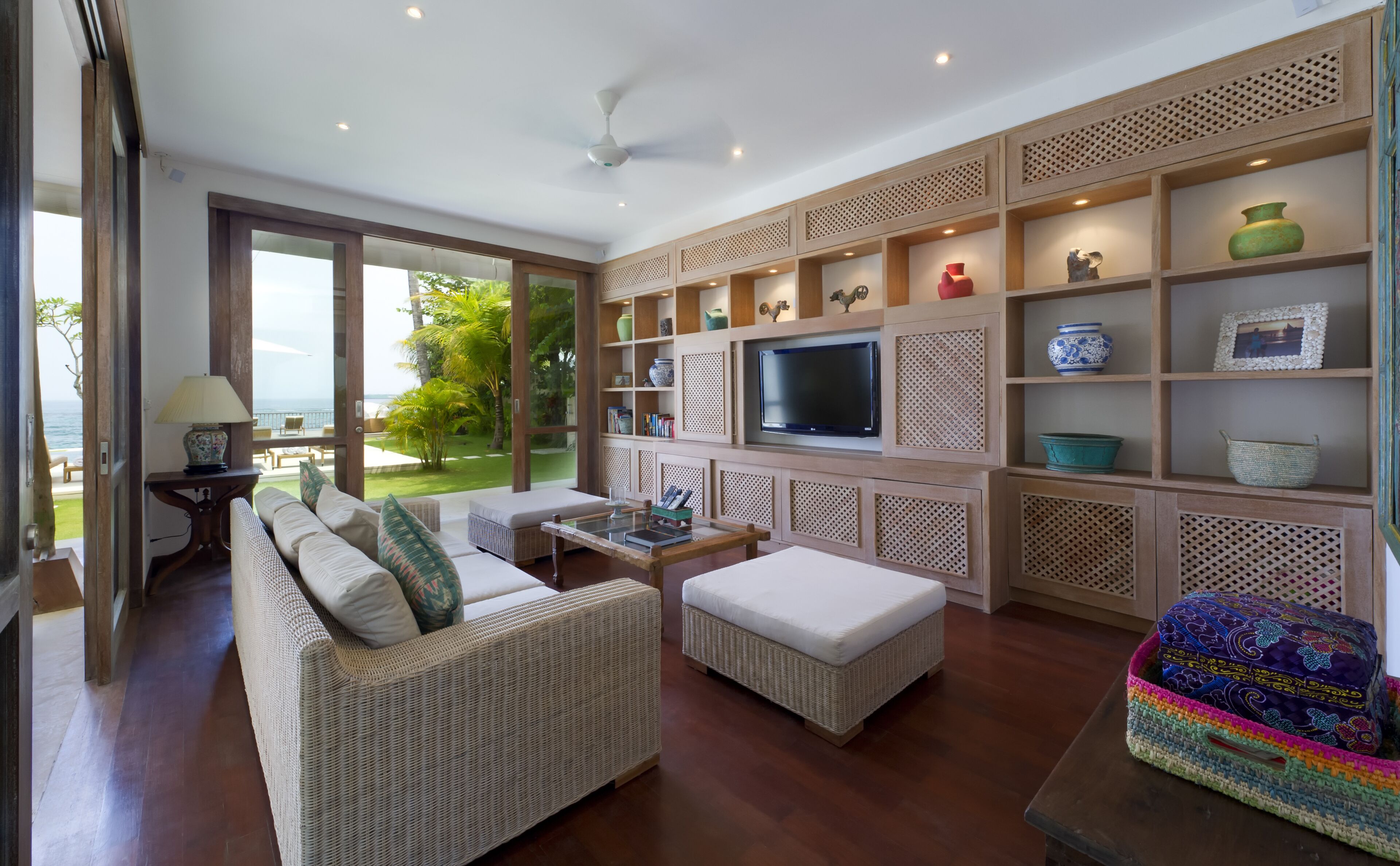 A spacious living room with a large TV, wicker furniture, and shelves with decorative items.