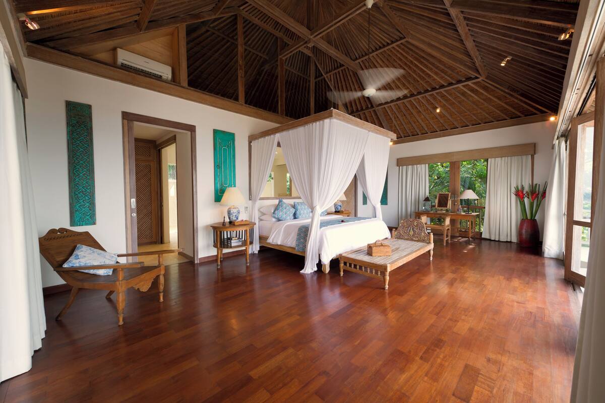 Um quarto espaçoso com cama de dossel, piso de madeira e ventilador de teto.