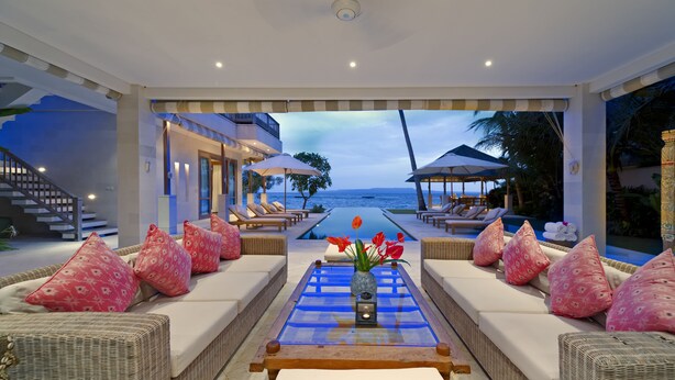 A poolside lounge area with wicker furniture, a glass-top table with a vase of flowers, and a view of the ocean. - Siri Mendira Beach Villas (Manggis)