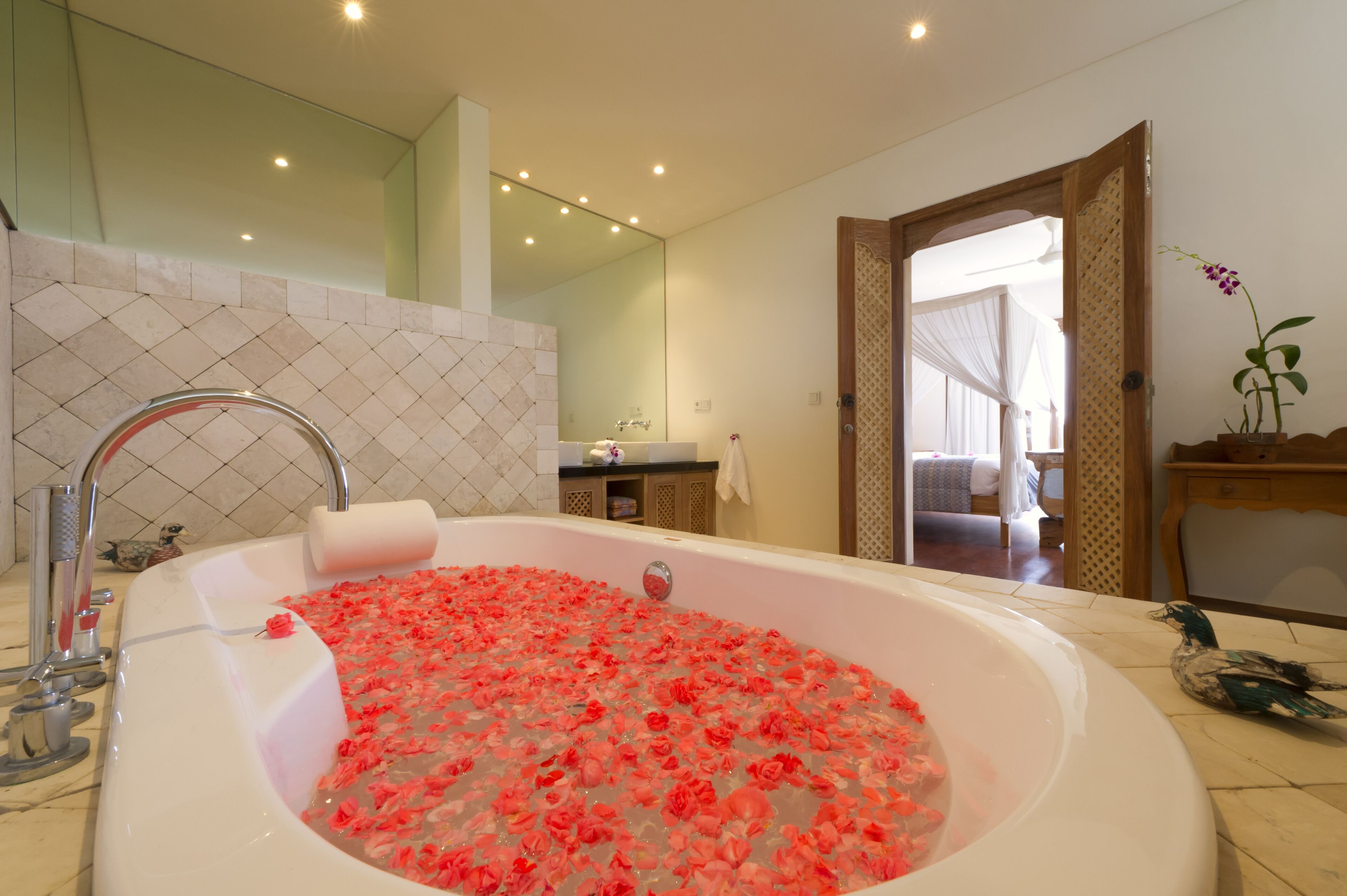 A bathroom with a large bathtub filled with rose petals, a mirror, a sink, and a shower area.
