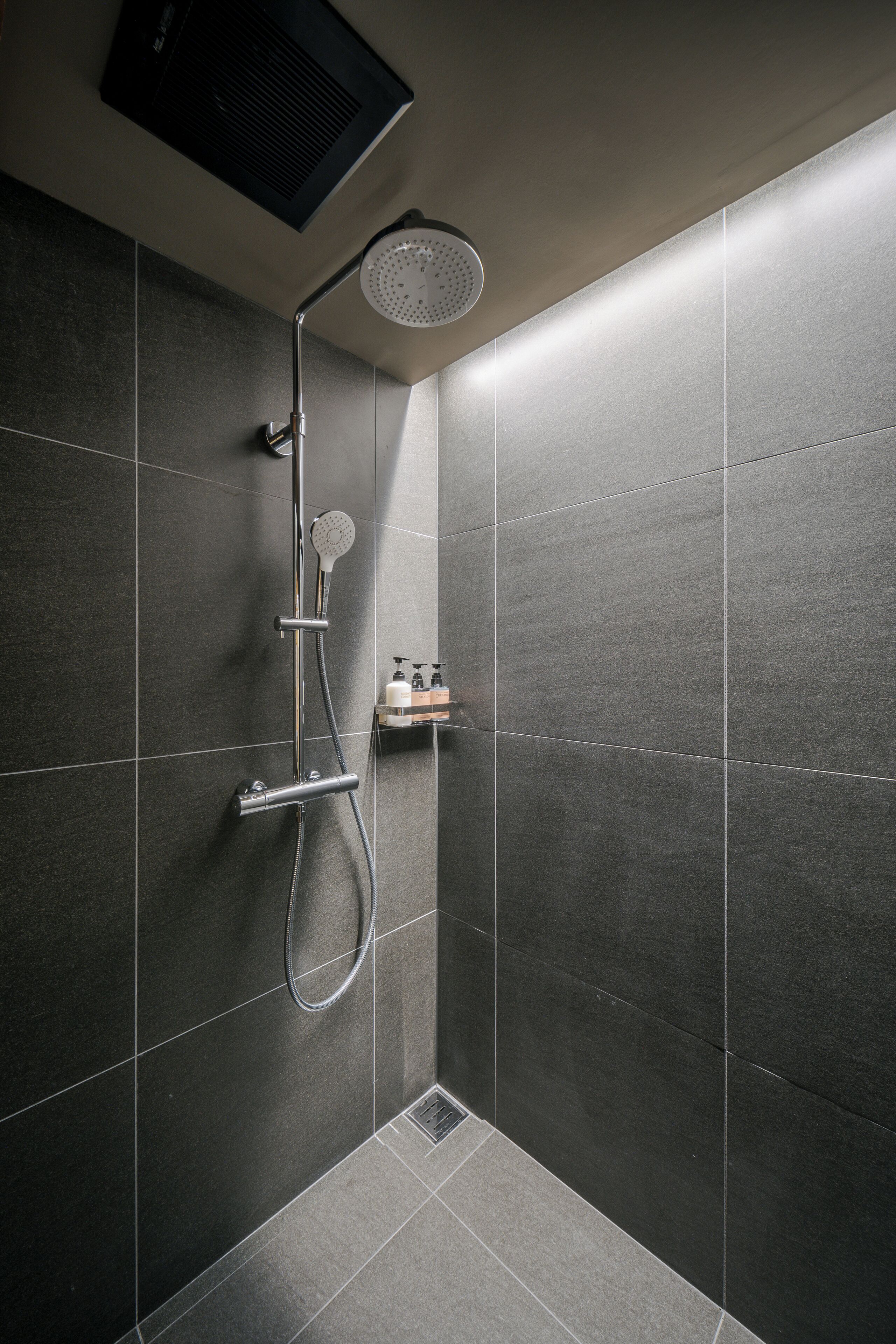 A modern shower with a handheld showerhead and a wall-mounted rain showerhead.