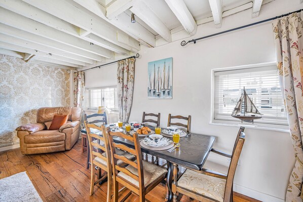 A dining area with a table set for four, surrounded by wooden chairs with cushioned seats. A leather sofa is positioned against the wall, and a painting of sailboats hangs above the table. - Fiddlers Green - Hamworthy, Poole (Poole)