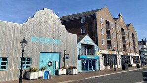 Een gebouw aan het water met een blauwe ingang en een bord waarop 'FISH AND CHIPS' staat.