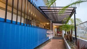 A building with a blue exterior, a covered walkway, and a row of palm trees. - Aoshima Loco Beach (Miyazaki)