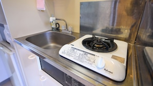 A kitchen with a white stove, stainless steel sink, and a pink towel hanging on the wall. - Aoshima Loco Beach (Miyazaki)