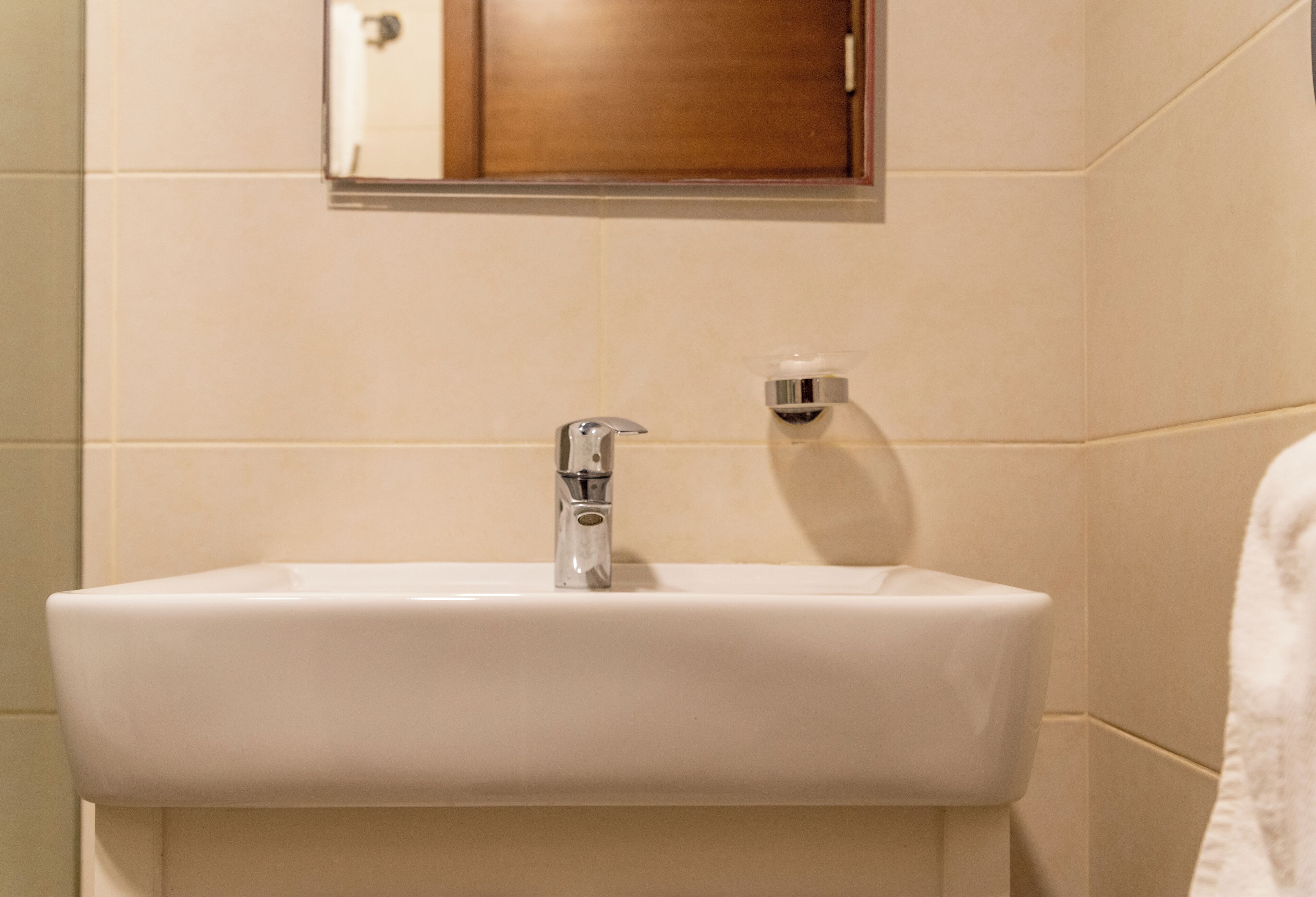 Une salle de bain avec un lavabo blanc, un miroir au-dessus et un porte-serviettes sur la droite.